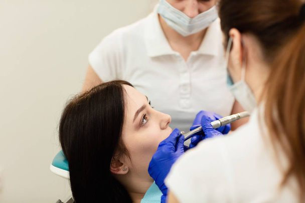 Closeup portrét mladé ženy, sedící v křesle na zubaře. Doktor zkoumá zuby. Zubní prevence - Fotografie, Obrázek