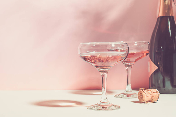 Шампанское или вино в элегантных бокалах на розовом фоне яркий свет. Принято. Селективный фокус
. - Фото, изображение