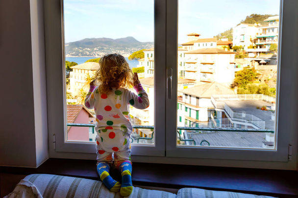 Kis kisgyermek lány gyermek élvezi kilátás ablakból reggel a Liguria régió Olaszországban. Cinque Terre és Portofino falvainak félelmetes falvai. Családi vakáció az olasz város színes házak. - Fotó, kép