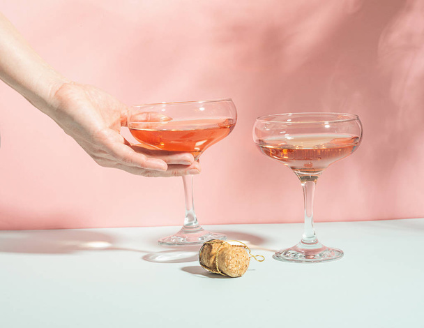 Female hand elegantly holding a glass of champagne or wine delicate pink background bright sunlight. Concept minimalism. - Photo, image