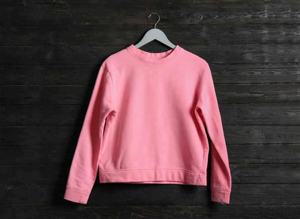 Hanger with pink sweatshirt on wooden background. Mockup for design - Fotó, kép