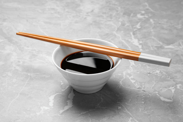 Bowl of soy sauce with chopsticks on marble background - Fotó, kép