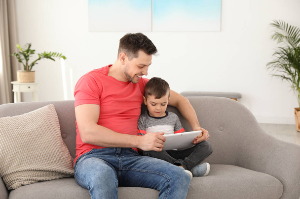Boy and his father with tablet sitting on sofa at home. Family time - Fotoğraf, Görsel