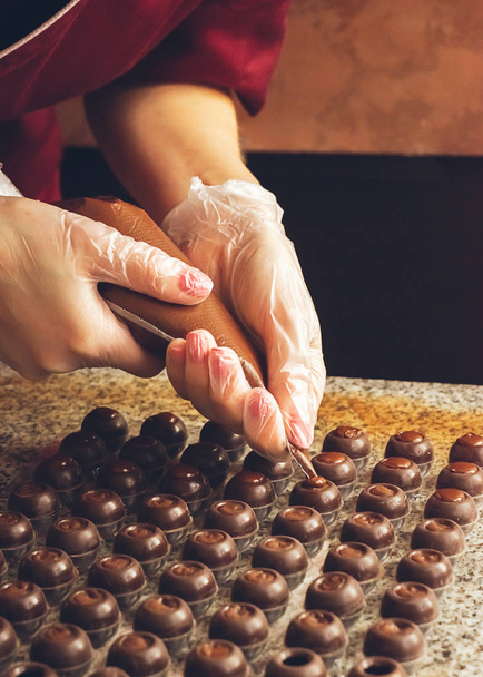 Φτιάχνω χειροποίητες σοκολάτες. Ένας ζαχαροπλάστης ρίχνει υγρή μαύρη σοκολάτα σε καλούπια. Γκρο πλαν. Επιλεκτική εστίαση. - Φωτογραφία, εικόνα