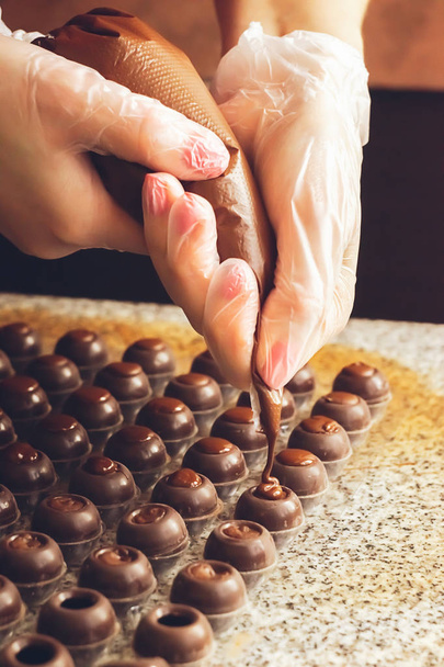 Het maken van handgemaakte chocolaatjes. Een banketbakker giet vloeibare donkere chocolade in mallen. Close-up. Selectieve focus. - Foto, afbeelding