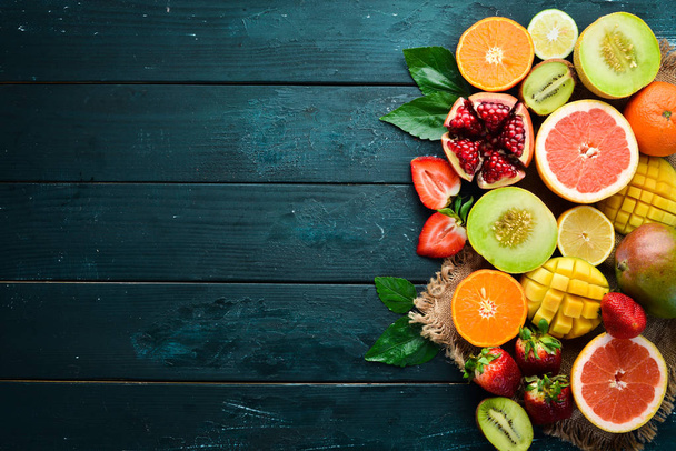 Fresh tropical fruits on a black background. Citrus, melon, pomegranate, strawberry, banana. Top view. Free space for your text. - Fotografie, Obrázek