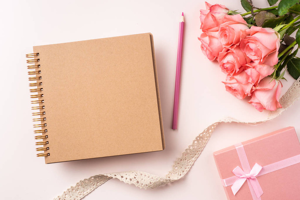 Kukkakimppu vaaleanpunaisia ruusuja, lahjapaketti, valkoinen muistikirja, lyijykynä ja vintage nauha vaaleanpunainen tausta
 - Valokuva, kuva