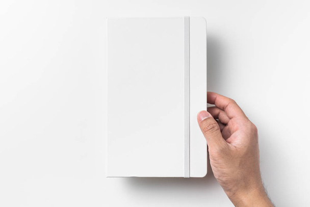 Male hand holding blank white notebook with elastic band isolated on white background. - Photo, Image