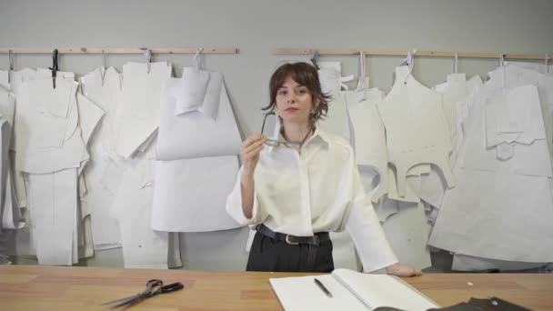 Female fashion designer smiling standing on background of paper patterns - Felvétel, videó