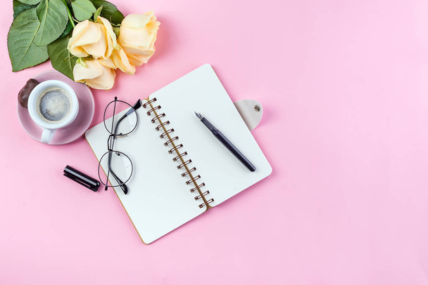 Morning coffee mug with glasses, empty notebook, pencil and rose on pink table top view . Woman working desk. - Foto, afbeelding