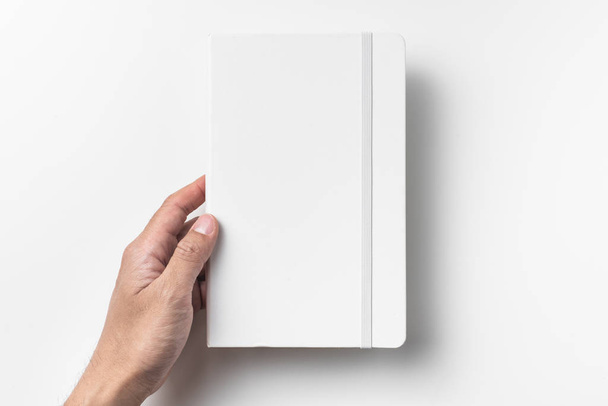 Male hand holding blank white notebook with elastic band isolated on white background. - Valokuva, kuva