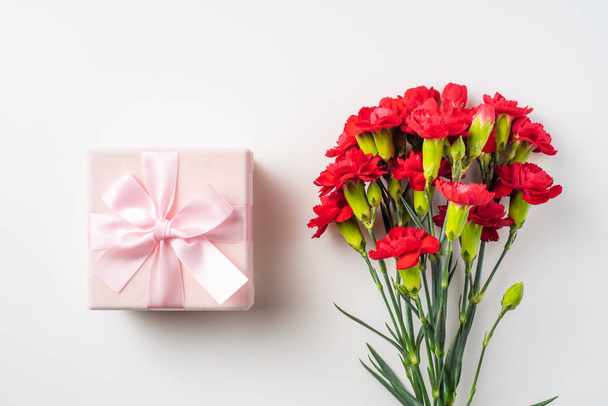 Bouquet of red carnations and gift box on background with copy space - Photo, image