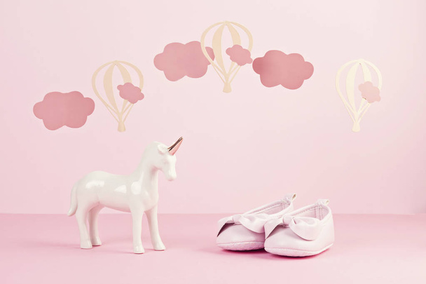 Malá roztomilá růžová obuv a jednorožec na růžovém pozadí s mraky a balony. Oslava narození dítěte, dívčí koncepce - Fotografie, Obrázek