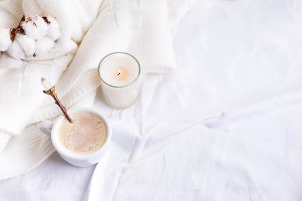 Roupa de cama com uma xadrez de malha macia e xícara de café, flores de algodão e vela. Dia aconchegante. Deitado plano, vista superior
 - Foto, Imagem