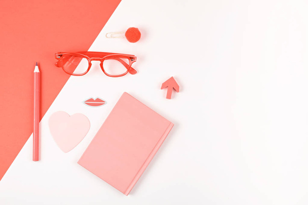 Top view of workspace with bullet journal, glasses and blogger accessories on colored coral background. Flatlay minimalism. Color of the year 2019 living Coral.  - Zdjęcie, obraz