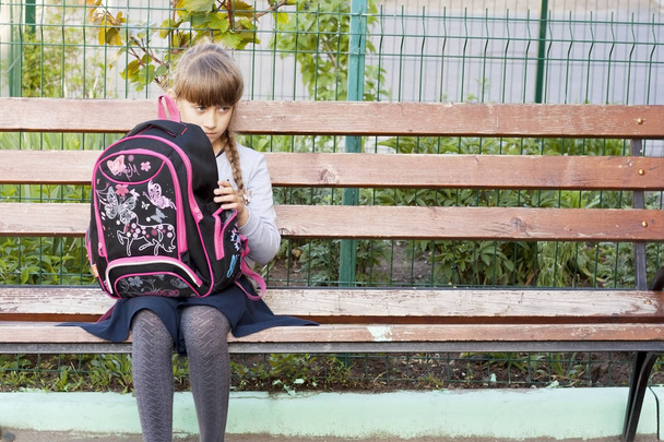 Україна, Одеса, 2019 травня сумна школярка з рожевим портфелем сидить на лавці у дворі. Освіта, концепція способу життя - Фото, зображення