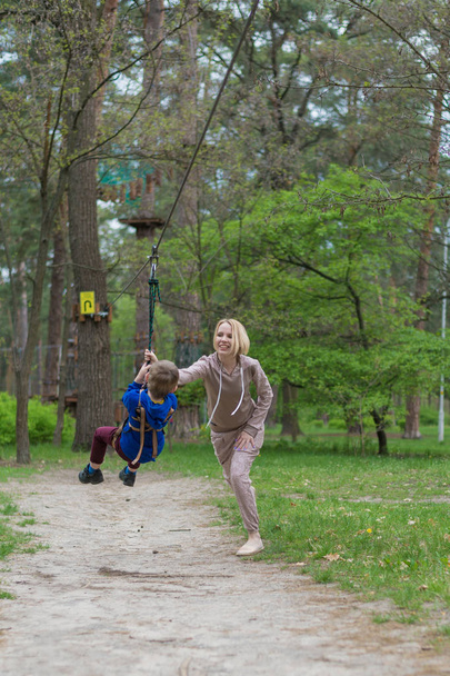 Moeder rolt haar zoon op de kabelbaan. Recreatieve activiteiten in het Park. Wederzijdse interactie tussen moeder en kind. - Foto, afbeelding