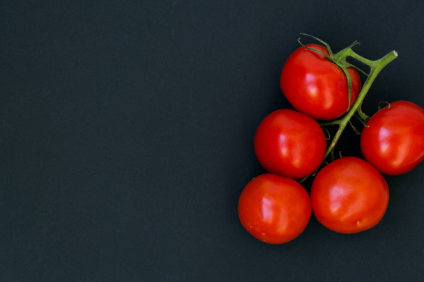 Organic red tomatoes with a green twig handful, lie on a black chalk board background. There is a place for text. - Foto, Bild