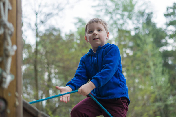 A little boy is training in a rope park. The child climbs the obstacle course. Active recreation in the park in the fresh air. - Foto, afbeelding