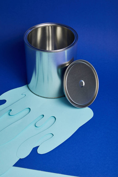 zilver glanzend kan en druipend papier gesneden verf op heldere blauwe achtergrond - Foto, afbeelding