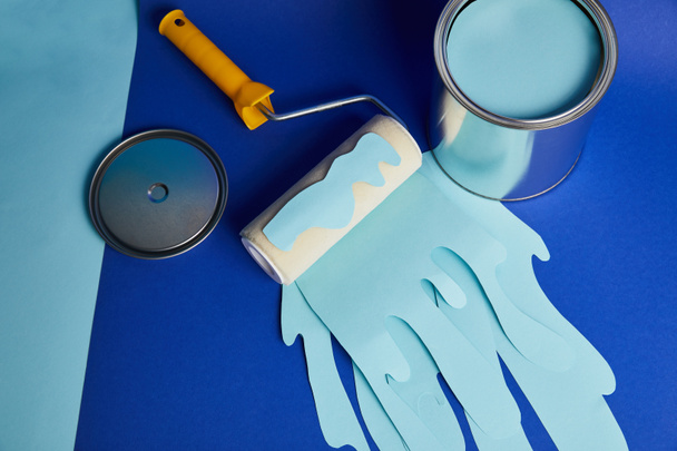 vista superior de lata de plata y rodillo con pintura cortada de papel goteante sobre fondo azul brillante
 - Foto, imagen