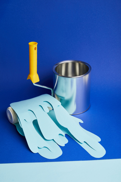empty metal shiny can near roller with dripping paper cut paint on bright blue background - Foto, Bild
