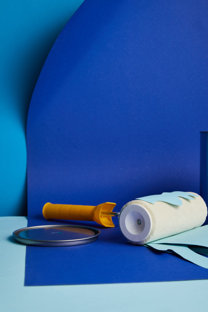metal cap near roller with dripping paper cut paint on bright blue background - Foto, afbeelding