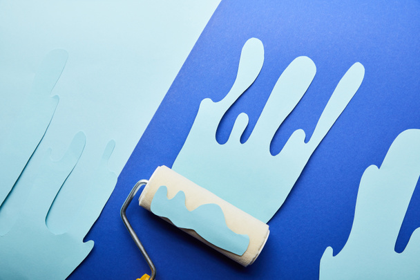 top view of roller with blue paper cut dripping paint on bright background - Photo, Image