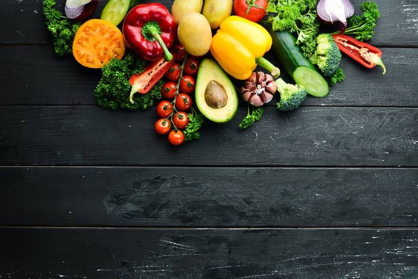 Fresh vegetables on a black background. Avocados, tomatoes, potatoes, paprika, citrus. Top view. Free space for your text. - Foto, afbeelding