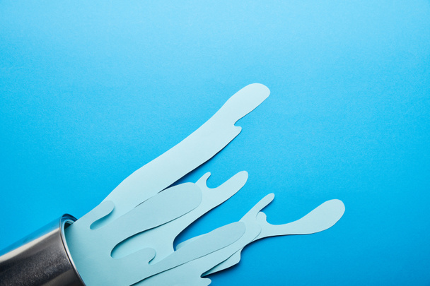 bovenaanzicht van metaal glanzend kan en morsen van papier gesneden verf op heldere blauwe achtergrond - Foto, afbeelding