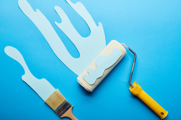 top view of roller and brush with dripping paper cut paint on bright blue background  - Photo, Image