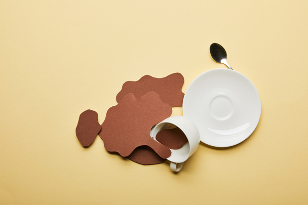 Draufsicht auf Papier geschnittenen Kaffee verschüttet in der Nähe von Tasse, Untertasse und Löffel auf beigem Hintergrund mit Kopierraum - Foto, Bild