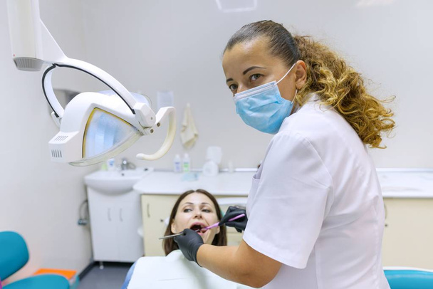 Portrait of positive mature female dentist treating patient in dental chair. - 写真・画像