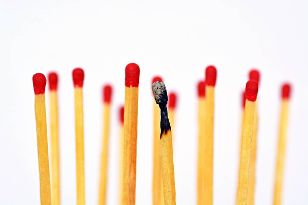 A burned match stands against a white background, next to it and behind are intact matches with a red heads. Concept for burnout and exhaustion - Фото, зображення