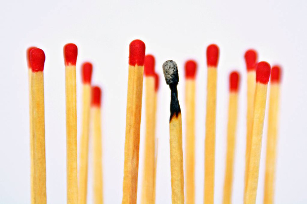 A burned match stands against a white background, next to it and behind are intact matches with a red heads. Concept for burnout and exhaustion - Foto, immagini