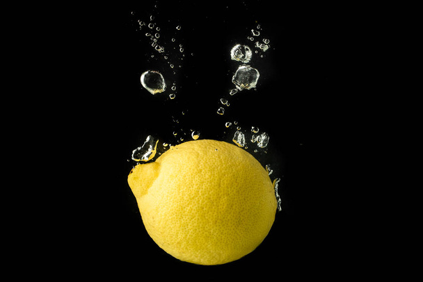 Lemon fruit splashing into water and sinking Isolated on black background - Foto, afbeelding