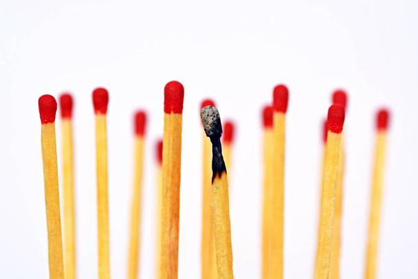 A burned match stands against a white background, next to it and behind are intact matches with a red heads. Concept for burnout and exhaustion - Fotografie, Obrázek