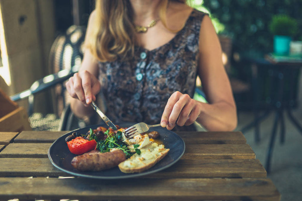 A young woman is having breakfast with sausage in a restaurant outdoors - Photo, Image
