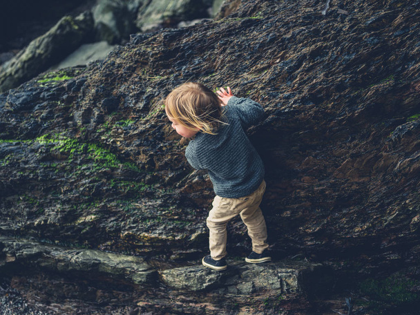 A little toddler is climbing rocks on the beach - Foto, afbeelding
