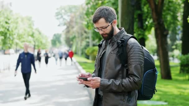 A szakállas férfit táska használja mobiltelefonnal az utcán - Felvétel, videó