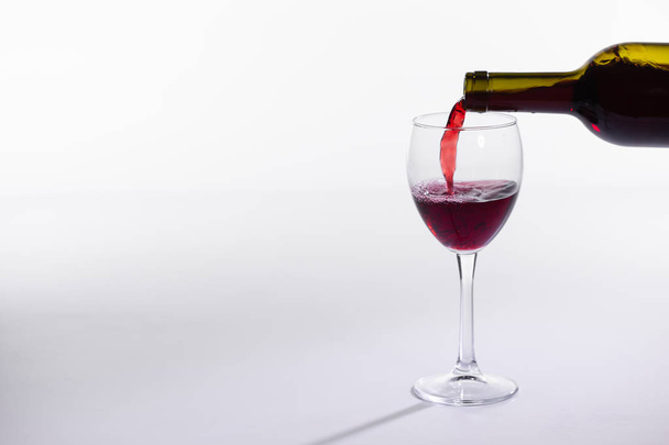 Červené víno vproudé do sklenice z láhve na bílém pozadí s prostorem pro kopírování - Fotografie, Obrázek