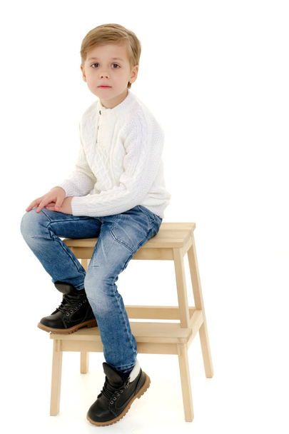 Een jongetje zit op een stoel. - Foto, afbeelding