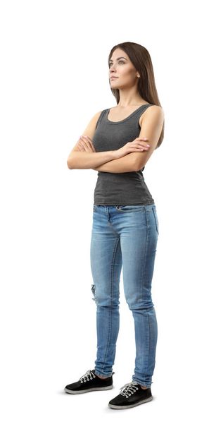 Young woman in gray top and blue jeans standing in half-turn with arms folded, looking up and away, isolated on white background. - Fotoğraf, Görsel