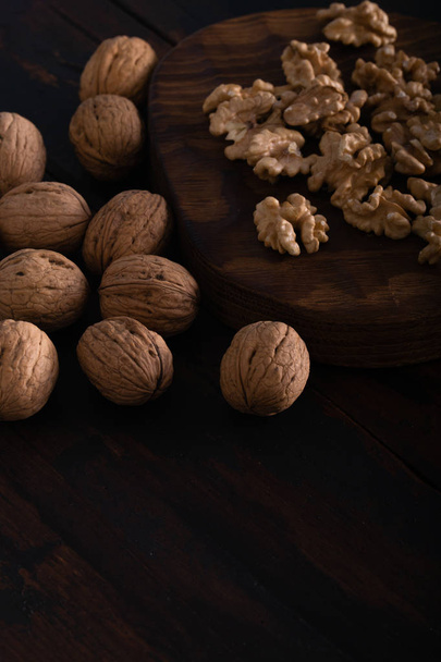 Cracked and whole walnuts on cutting board and wooden black table, side view. Healthy nuts and seeds composition. - Foto, Imagem