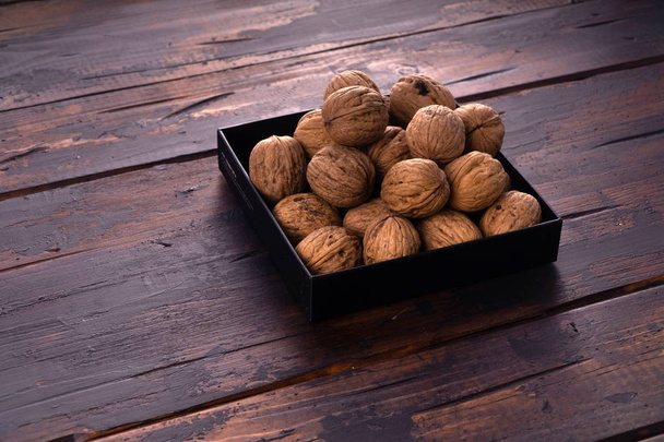 Whole walnuts on a square plate on wooden table, side view. Healthy nuts and seeds composition. - Foto, Imagem