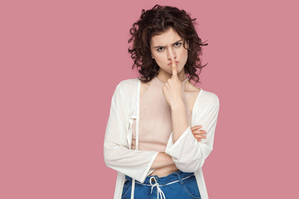 angry beautiful brunette young woman with curly hairstyle in casual style looking at camera and showing lie sign on pink background - Foto, Bild