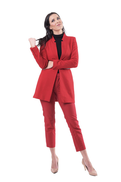 Feliz joven mujer de negocios en traje rojo tocando el pelo pensando y mirando hacia arriba teniendo idea. Cuerpo completo aislado sobre fondo blanco
. - Foto, Imagen
