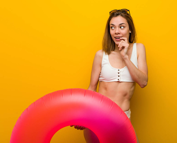 Mujer joven con bikini sosteniendo una dona inflable relajado pensando en algo mirando un espacio de copia
. - Foto, Imagen