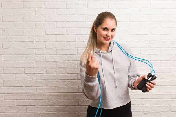 Young fitness russian woman holding a jump rope against a bricks - Photo, Image