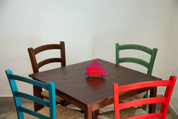 Puinen pöytä värikkäillä tuoleilla ravintolassa. Käytetään perinteisissä kahviloissa, tavernoissa, bistroissa, pubeissa, kahviloissa. Kuva neljä tuolia ja pöytä
. - Valokuva, kuva
